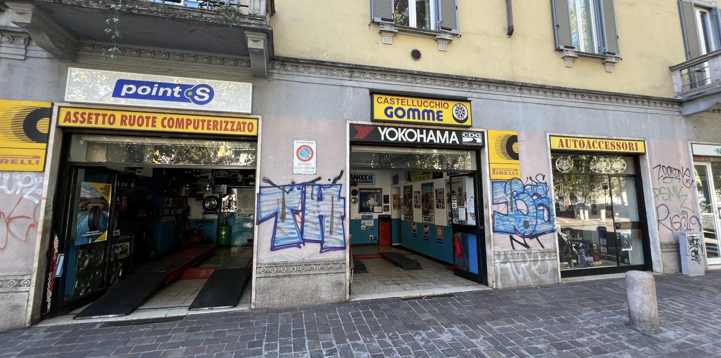 La fronte completa del negozio sull'angolo tra Via Passeroni e Corso Lodi: le due campate dell'officina aperte e la vetrina degli accessori