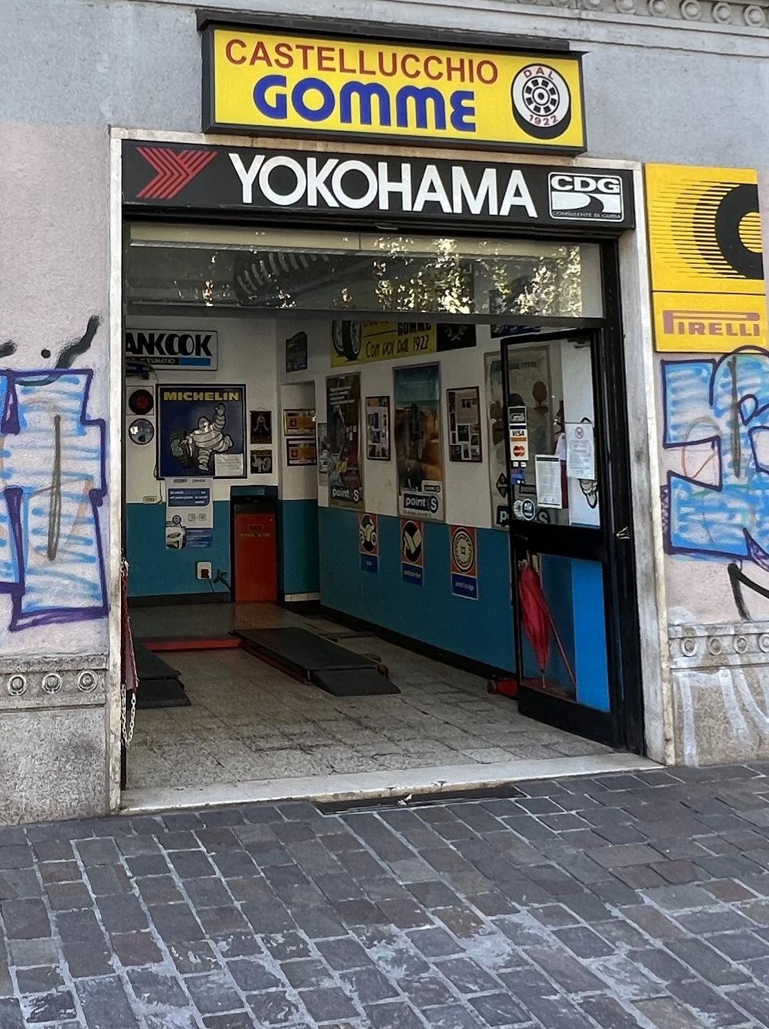 L'ingresso di IL GOMMISTA in Via Passeroni 1 a Milano: l'insegna gialla «Castellucchio Gomme dal 1922», il bandone Yokohama e la campata aperta dell'officina