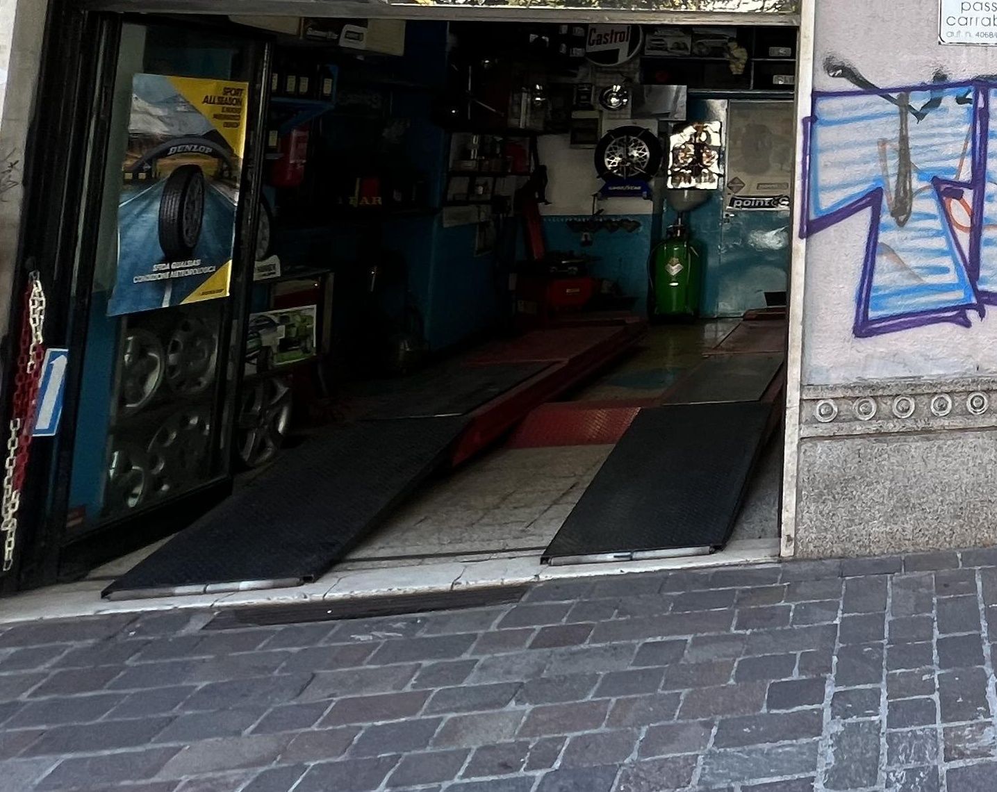 La campata dell'officina vista dalla strada, con le pedane pronte davanti all'ingresso e la parete azzurra piena d'attrezzi
